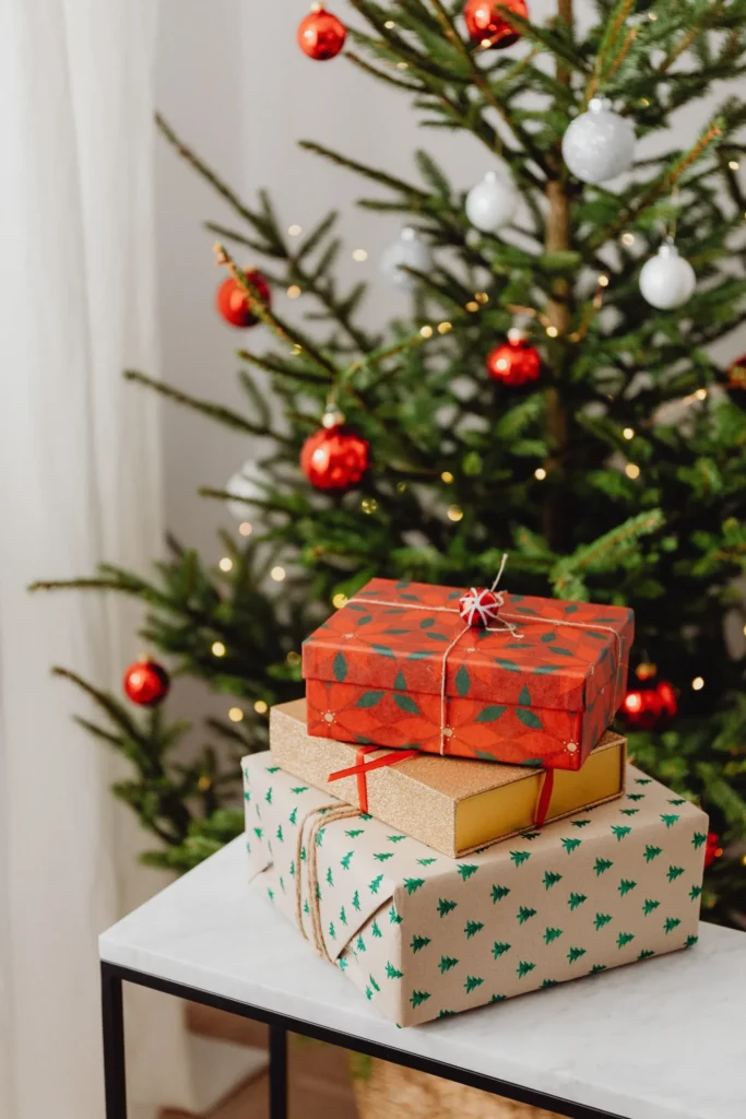 Decorated Christmas tree with red and white ornaments behind three stacked wrapped gifts