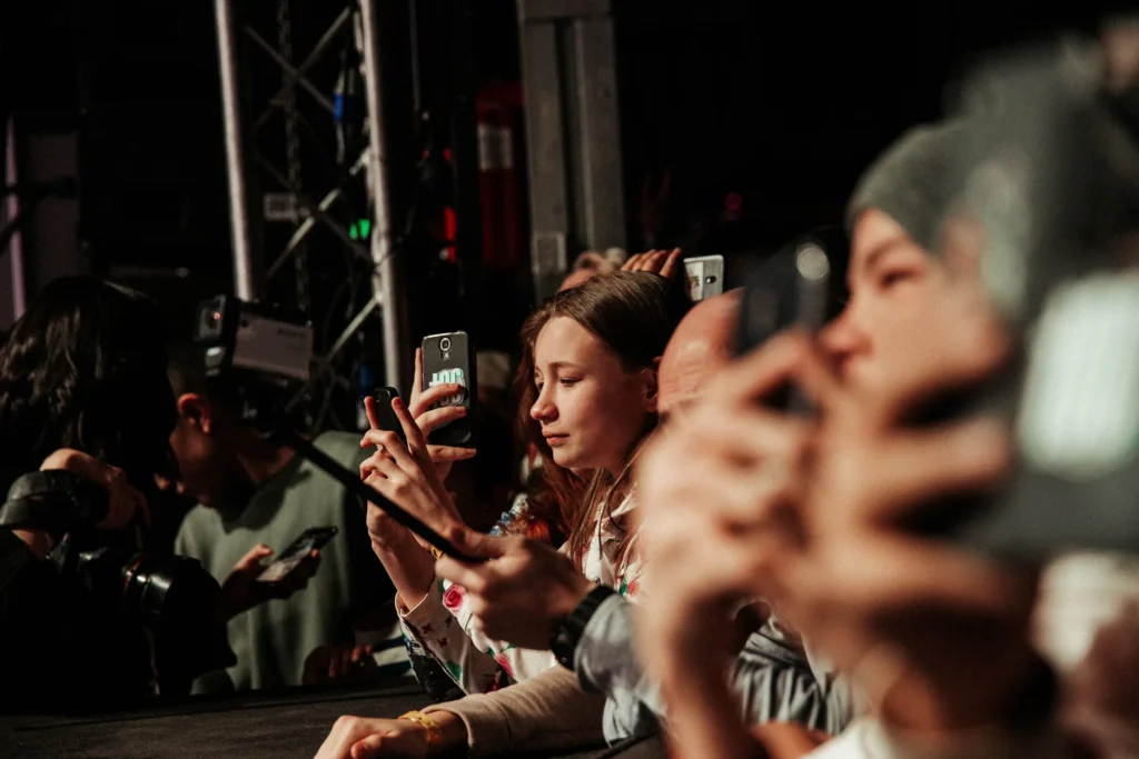 Audience members raise smartphones and cameras at an indoor event