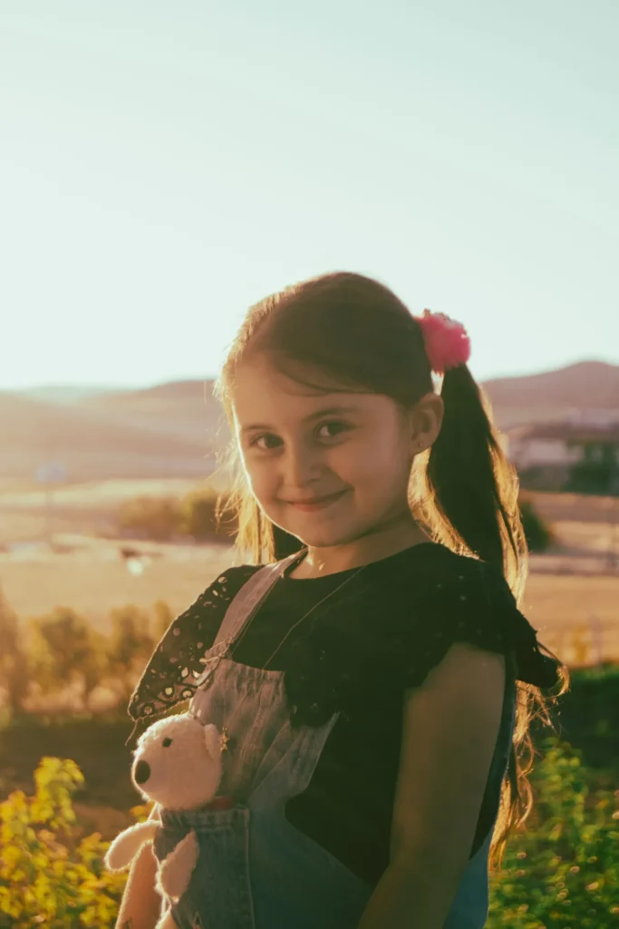 Smiling girl with a teddy bear in her pocket at sunset